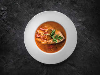 Fish soup in white plate on dark background. Overhead view.
