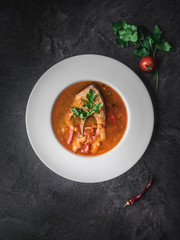 Fish soup in white plate on dark background. Overhead view.