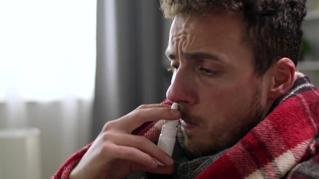 Ill man uses nasal spray on sofa in living room