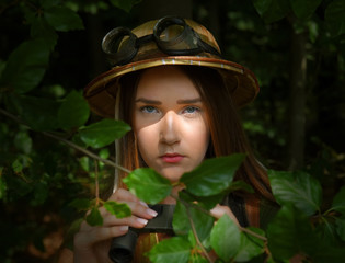 A young girl dresses up as an explorer. She wears a jungle hat and is seen in a forest environment.