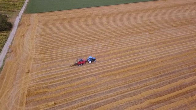 Vista aerea della Raccolta del fieno di grano in baloni quadri con una pressa ultra moderna ed un trattore da 250 cavalli 