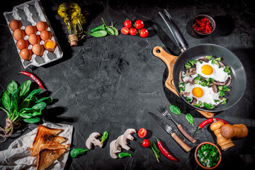 Delicious breakfast or snack: scrambled eggs, bacon, mushrooms, green onions, toast and tomatoes on dark background. Top view with copy space