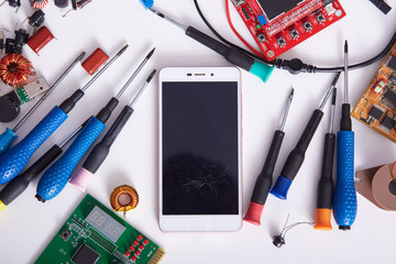 Smartphone, motherboards and tools laying on white back table, radiotrician workspace. Computer...