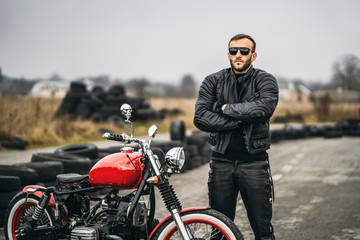 Red motorbike with rider. A man in a black leather jacket and pants stands near a motorcycle with...