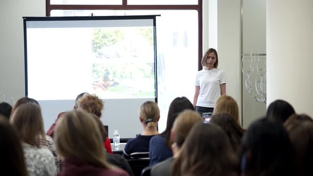 Rear view of unrecognized participant in audience. Female speaker giving talk at corporate business conference