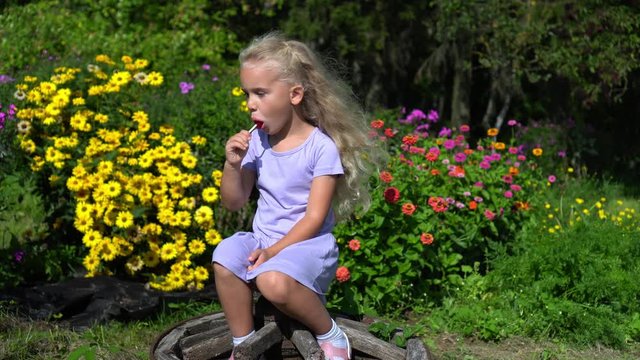Cute blond girl sitting on retro wheel between colorful zinnia flowers