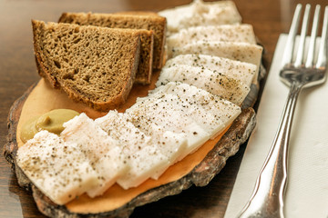 Cut fresh fat with black bread on the wooden board serving in restaurant.