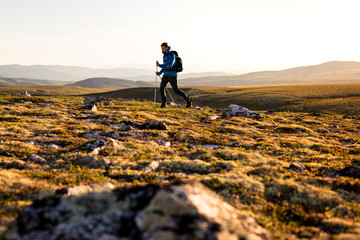 Rondane National Park, Norway: A male hiker hiking on a trail from the parking in Spranget towards Rondvassbu in the evening light.
