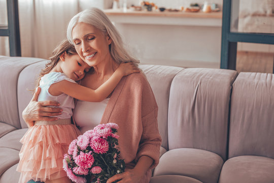 girl sitting on the grandmothers laps holding bouquet of flowers at home