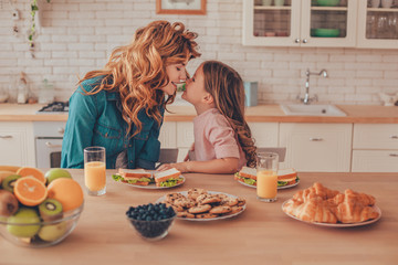 side view of daughter and mother touching noses while sitting at the kitchen table with food