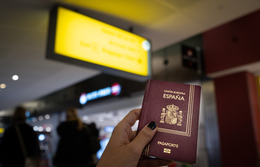 Fototapeta premium Close up of woman holding a Spanish passport over a blurred airport background