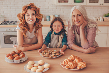 cheerful girl, young woman and senior woman smiling at the camera on the kitchen with baked products on the table
