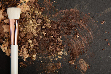 White make up brush and brown and gold eyeshadows arranged on flat stone.