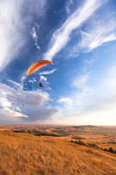 A male paraglider paraglides above rolling farm lands at sunset near Moscow, Idaho.