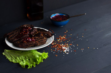 fresh grilled steaks, wild meat with spices on a black background, the concept of food with no GMOs