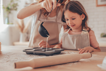 daughter and mother pouring batter with ladle into the form for cupcakes
