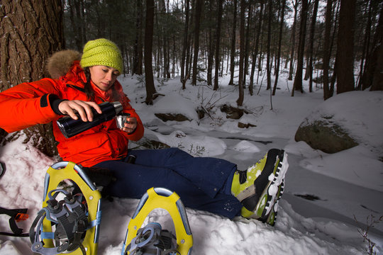 A woman admires the view of a frozen brook while taking a break from snowshoeing to have hot tea in the Green Hills Preserve near North Conway, New Hampsire.