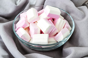 White pink fluffy marshmallows in a glass bowl on a gray picturesque flowing fabric. Sweet and tasty winter food. Close-up delicious soft sweets.