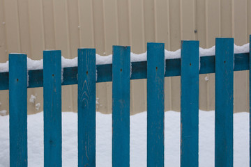 Abstract background in the form of a blue wooden fence on a background of beige profiled sheet and snowdrift in winter.
