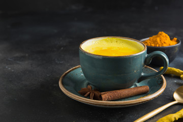 Cup of golden turmeric latte milk on dark. Close up.