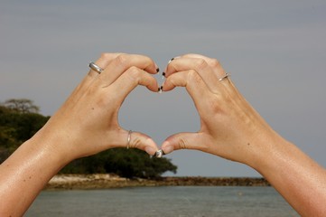 Female hand making a heart shape against a beautiful blue sky