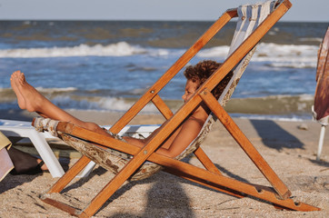 tanned baby boy resting and sunbathing in a deck chair on the sand by the blue sea