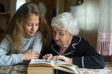 Elderly woman granny is reading a book to her beloved granddaughter.