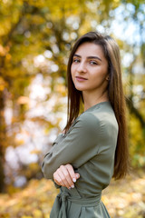 Autumn park. Beautiful woman in green dress posing in autumn park with yellow leaves