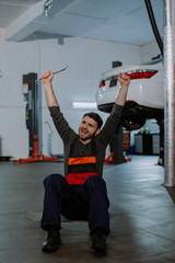 A young mechanic is sitting on a skateboard, showing hands at the camera very happy