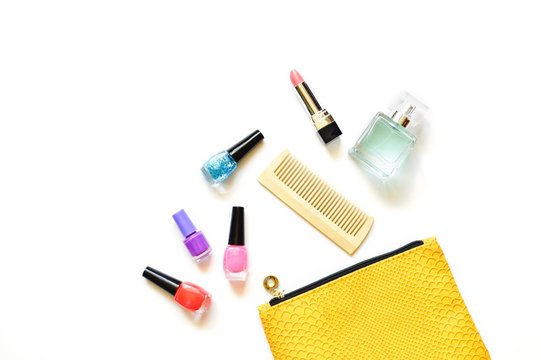 Colorful nail polishes, comb, pink lipstick and perfume. The contents of a yellow cosmetic bag. Flat lay beauty photography