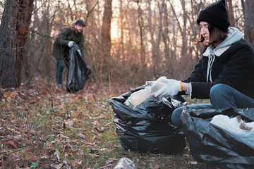 People clean up the forest of plastic trash. Environmental awareness concept: man and woman picking...