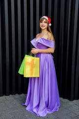 New year celebration. Happy woman in fashion evening dress with gift colorful bags in santa hat