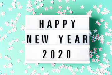 Glowing neon light box on the mint green background with the inscription Happy New Year 2020. Trendy neo color composition with silver stars