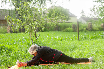 An elderly woman of 90 years old, with gray hair and a headband, makes a longitudinal split in the...