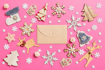 Fototapeta na wymiar Top view of craft envelope on pink background made of holiday decorations and toys. Christmas ornament concept