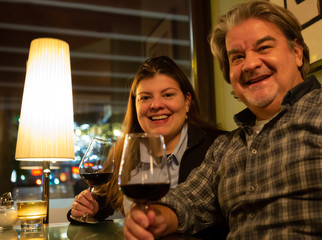 Couple enjoying glass of wine poses smiling for a photo.