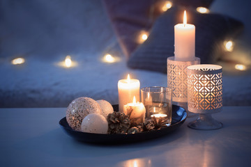 Christmas decoration   with burning candles on  white table against the background of  sofa with plaids and pillows. Cozy home and holiday concept