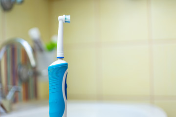 A modern electric toothbrush in white and blue colour stands on the edge of the bathroom sink.