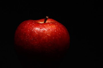 Appetizing red apple covered with drops of water on a black background. Close-up