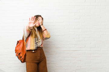 young pretty woman covering face with hand and putting other hand up front to stop camera, refusing...