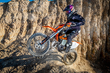 Image of a female dirt biker jumping up a rocky section of trail - obrazy, fototapety, plakaty
