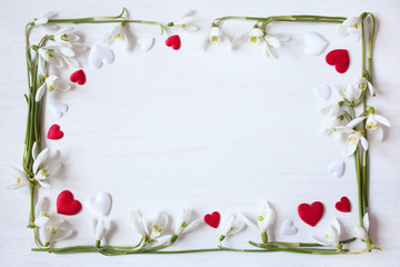 White wooden background with spring snowdrops and red and white hearts.