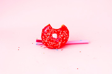 Bitten colored donut with colorful sprinkles and toothbrush on pink background. Copy space