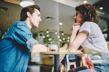 Young serious man attentively listening girlfriend during date in modern cafe interior, hipster guys communicating with each other and discussing common startup during friendly meeting in coffee shop