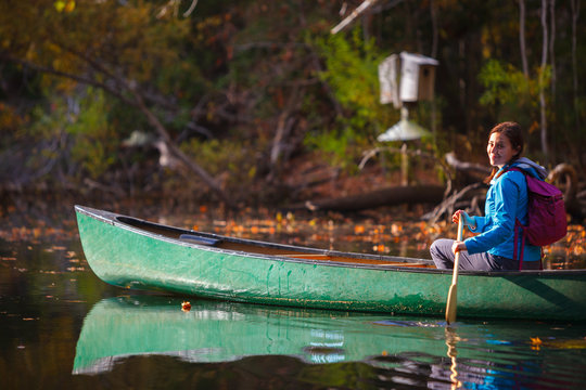 A woman canoeing on the still waters of a freshwater pond along the Discovery Trail during a sunny autumn afternoon at the Nags Head Woods Preserve.