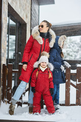 A young mother with her tree children have a fun and playing snowballs outdoor near the home