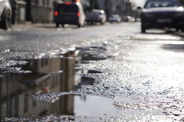 Sunny street after the rain. reflection, glare of the sun in puddles and wet asphalt, asphalt with...