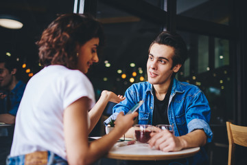 Couple in love resting together in cafe and discussing new video in blog on smartphone device during meeting in cafe.Hipster guys dressed in casual wear communicating with each other in cafe