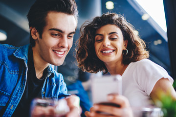 Cheerful young man and woman discussing funny video in blog holding smartphone device.Positive...