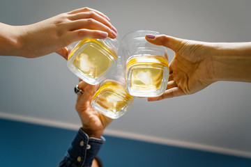 Close up on three female women hands holding a glasses of whiskey or brandy or cognac alcohol drink toasting celebrating at home low angle view